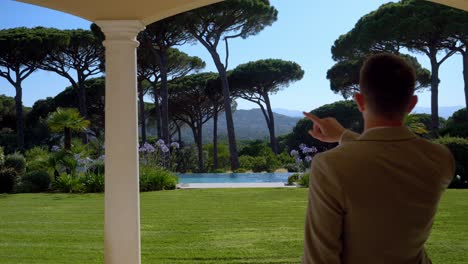 Dolly-forward-shot-businessman-showing-own-luxury-garden-with-swimming-pools-and-pine-trees