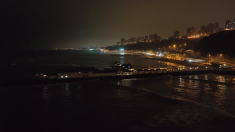 Aerial:-Night-pier-restaurant,-highway-traffic-below-Lima-Peru-cliffs