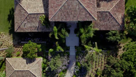 Aerial-top-down-shot-of-person-entering-luxury-villa-during-sunny-day-with-tropical-large-garden