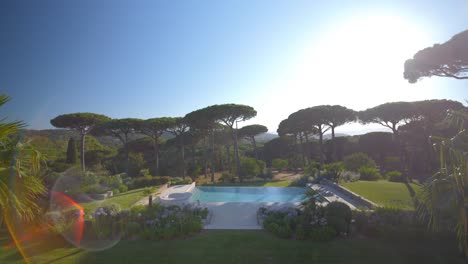 Dolly-forward-shot-of-luxury-swimming-pool-and-pine-trees-in-garden-during-sunlight