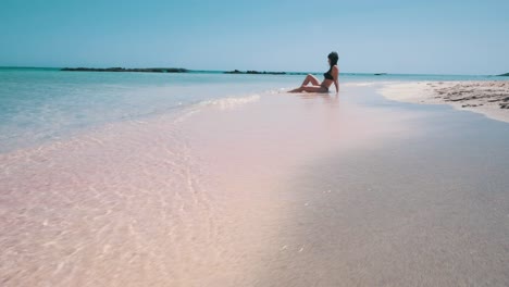 A-woman-sitting-on-a-pink-beach-in-front-of-the-turquoise-lagoon