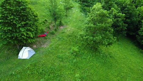 Chilling-on-hammock-near-waterproof-tent-in-the-forest-drone-circle-shot