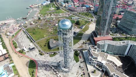 Bright-sunshine-reflects-on-Alphabet-tower-in-Batumi-city,-aerial-view