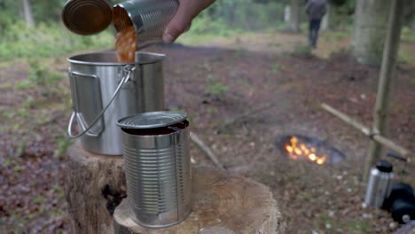 Male-pouring-baked-beans-into-a-pot-in-the-forest,-Static-Shot
