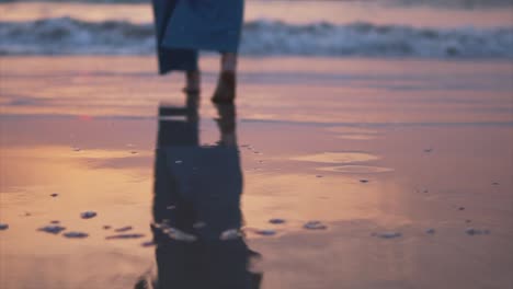 Young-woman-in-blue-pants-walking-alone-on-the-beach-in-the-sunset