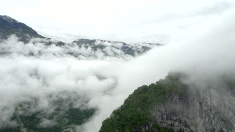 Drone-flight-above-fjord---valley-filled-with-clouds-panning-down-as-getting-closer-to-the-end-of-Cliff