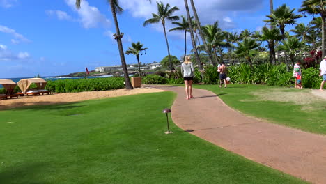 Young-blonde-woman-walks-away-from-camera-at-lushly-manicured-resort-hotel-in-Poipu-Beach,-Garden-Isle,-Kauai,-Hawaii-4k