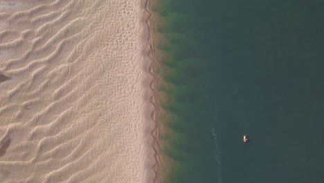 A-lone-kayak-paddling-along-the-stunning-golden-sandy-shoreline,-top-down