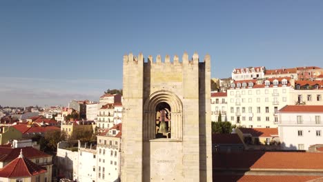 Up-and-away-drone-flight-over-the-belfry-of-the-Catedral-Sé-Patriarcal-Igreja-de-Santa-Maria-Maior-in-Lisbon-Portugal-Alfama-Europe-ob-a-blue-sky-day