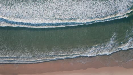 Top-down-on-waves-rolling-onto-the-beach-with-multicolored-sections