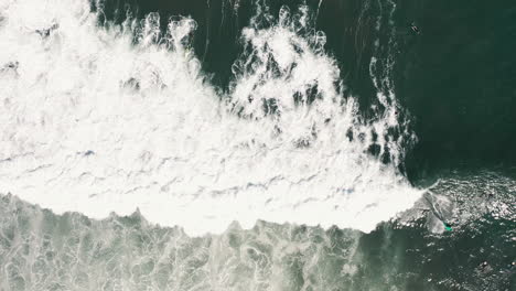 Top-down-aerial-drone-shot-of-people-surfing-and-trying-to-catch-waves-in-white-water-of-the-Spanish-coast