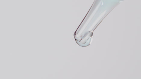 Close-up-of-transparent-liquid-droplets-slowly-falling-on-white-background