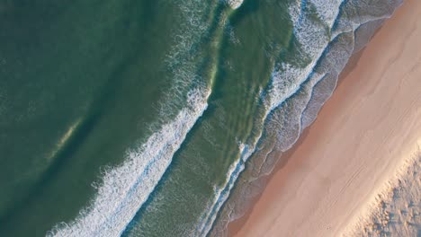 Foamy-ocean-waves-hitting-sandy-beach,-aerial-top-down-view