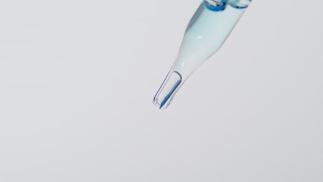 Transparent-liquid-falling-from-glass-pipette,-close-up-view-isolated-on-white-background