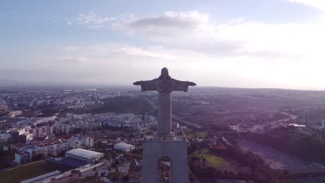 Stationärer-Und-Sich-Nähernder-Drohnenflug-Zum-Gesicht-Von-Christus-Cristo-Rei-In-Portugal-Lissabon-Bei-Sonnenuntergang-Mit-Stadt-Im-Rücken