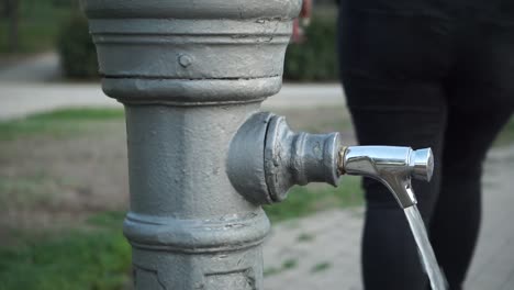 Woman-turns-on-public-water-tap-in-park,-slow-motion-close-up