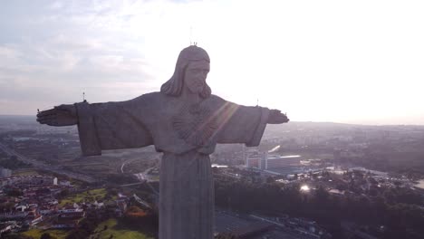 Drone-Descendiendo-Lentamente-Con-La-Estatua-Cristo-Rei-De-Jesucristo-Frente-Al-Sol-Poniente-En-Portugal-Lisboa