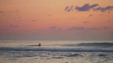 man-wearing-wetsuit-paddling-flat-on-surfboard-in-the-ocean-at-sunset