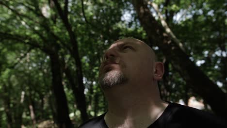 A-man-stands-in-forest-looking-up-at-sky-in-slow-motion