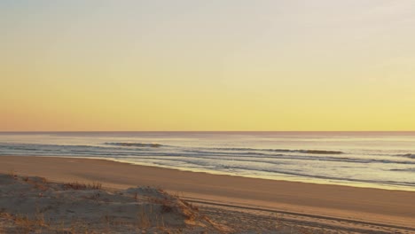 View-of-the-waves-and-beach-from-sand-dune-during-colorful-yellow-tones-sunset