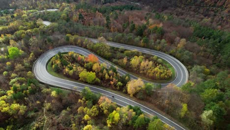 Beautiful-aerial-view-of-a-winding-road-surrounded-by-a-wonderful-forest-in-autumn
