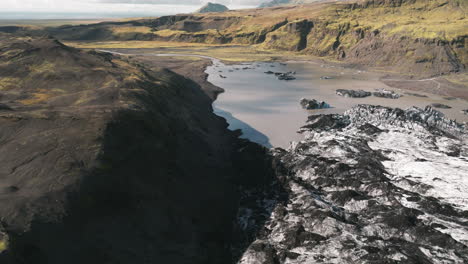Right-to-left-aerial-sliding-shot-of-receding-Iceland-glacier,-silty-pond