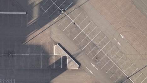 Empty-asphalt-parking-lot-with-white-lines-and-tire-marks,-aerial-top-down-ascend-and-spin-view