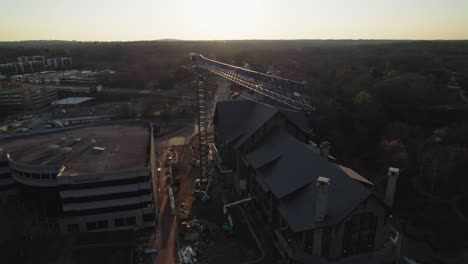 Drone-orbiting-crane-on-building-site-in-morning-sun-with-busy-road-in-background