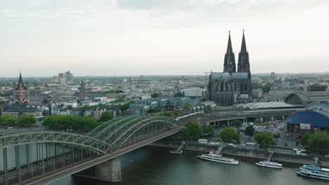 Drone-moves-to-the-right,-the-Cologne-Cathedral-in-gloomy-weather-is-in-the-center,-the-Hohenzoller-Bridge-with-the-Rhine-is-in-the-lower-part-of-the-picture