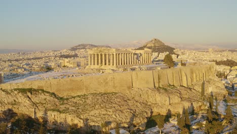 Aerial-view-over-the-Acropolis-hill,-revealing-the-snowy-cityscape-of-Athens,-golden-hour-in-Greece---rising,-drone-shot