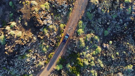 Black-color-car-driving-on-dirt-road-in-rocky-mountain-landscape,-aerial-top-down-view