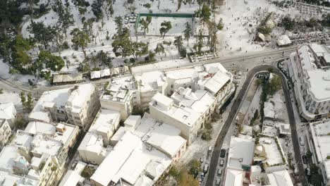 Aerial-view-overlooking-snowy-house-roofs-and-historic-ruins,-in-sunny-Athens,-Greece---high-angle,-drone-shot