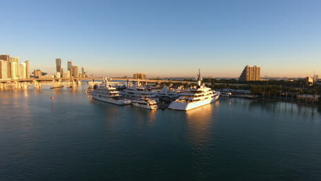 Yachts-docked-on-port-in-dockyard-near-a-city-|-cityscape-skyline-video-during-sunset-with-golden-lights-on-buildings-|-Yachts-docked-on-port-in-bay-near-a-city
