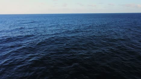 Vibrante-Agua-Oceánica-De-Color-Azul-Oscuro-Con-Un-Horizonte-Infinito,-Vista-Hacia-Atrás-De-La-Mosca-Aérea