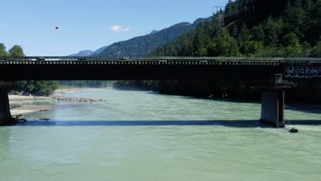 Atemberaubender-Drohnen-Dolly-Unter-Einer-Brücke-über-Einem-Türkisfarbenen-Fluss