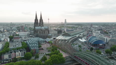 Drone-films-in-Slowmotion-the-Cologne-Cathedral,-the-Cologne-Central-Station,-the-Cologne-Theather-in-the-sunset,-the-drone-moves-down-and-the-Rhine-with-the-Hohenzoller-Bridge-comes-into-the-picture