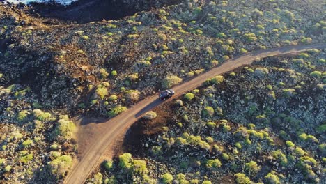 Black-vehicle-driving-on-dirt-coastal-road-on-rocky-terrain-in-Lanzarote-island,-aerial-view