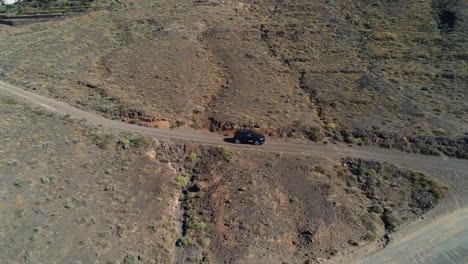 Dark-SUV-driving-down-dirt-mountain-road-in-Lanzarote,-Spain,-aerial-view