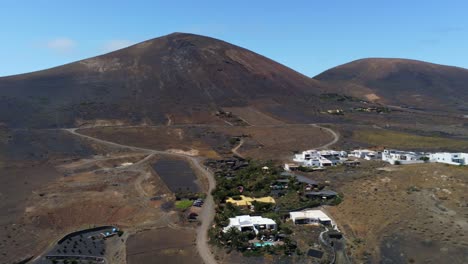 Rural-road-and-small-village-near-majestic-mountain-in-Lanzarote,-aerial-drone-view