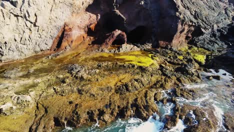 Natural-formation-cave-near-rocky-coastline-of-Lanzarote-island,-aerial-fly-back-view