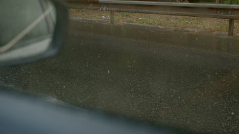 Vehicle-driving-on-wet-asphalt-during-rainfall,-side-view-from-inside-car