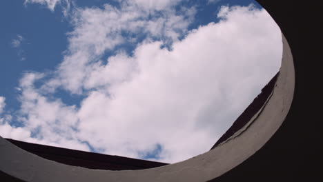 A-Bird-Gliding-With-Spread-Wings-Against-Cloudy-Blue-Sky-Viewed-From-An-Ancient-Building-Roof-With-Opening-Hole