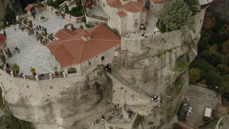 Aerial-view-over-the-Monastery-Varlaám-full-of-tourists,-in-Meteora,-Greece---rising,-high-angle,-drone-shot