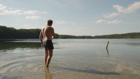 Adult-Guy-Standing-On-Lakeshore-Throwing-Stone-In-Peaceful-Water-Of-Jezioro-Glebokie,-Poland