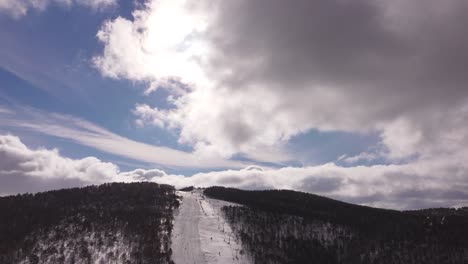 Drone-flying-over-ski-resort-with-beautiful-clouds-and-sun
