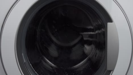 Close-up-static-shot-of-washing-machine-washing-dark-clothes