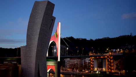 Modern-design-of-the-La-Salve-bridge-for-pedestrians-and-cars-at-night-in-Bilbao-Spain-illuminated,-Wide-handheld-shot