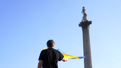 London-stands-with-Ukraine,-protester-waving-the-Ukrainian-flag-in-Trafalgar-Square-in-London-during-protest-against-war-with-Russia
