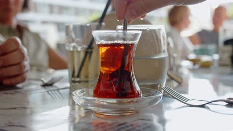 Person-takes-spoon-and-spin-it-in-cup-of-tea-while-sitting-at-restaurant,-close-up-view