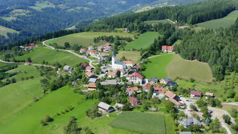 Aerial-circling-shot-above-a-small-village-with-church-in-the-middle-in-Prevalje,-slovenia